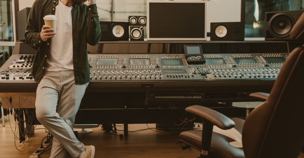 young sound producer standing at studio with cup of coffee to go